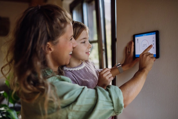 Eine Person mit Kind im Arm stellt ein Thermostat ein